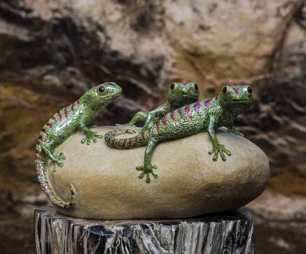 A figurative ceramic stoneware sculpture of three green geckos on top of a rock.