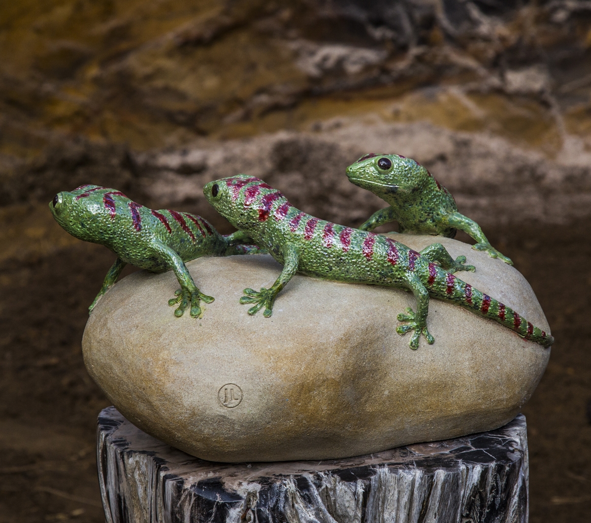 A figurative ceramic stoneware sculpture of three green geckos on top of a rock.