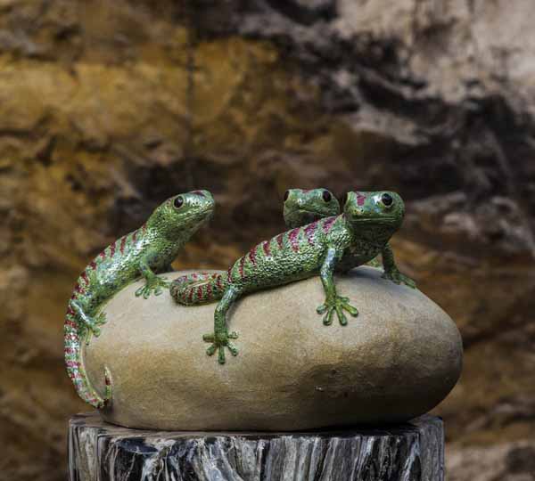 A figurative ceramic stoneware sculpture of three green geckos on top of a rock.