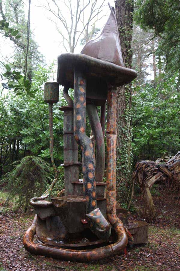 A abstract welded steel sculpture of a large structure with a snake-like shape around it.