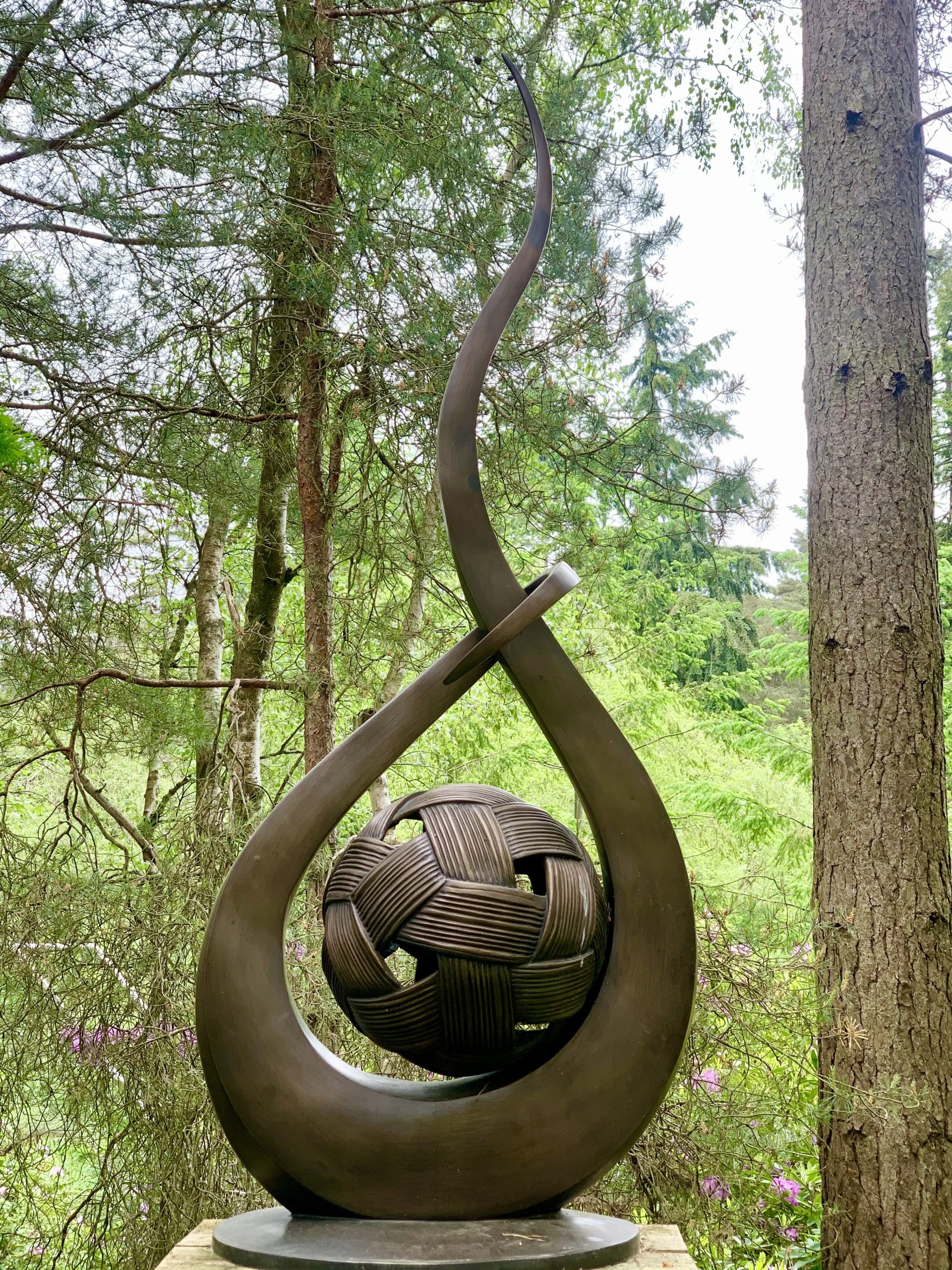 A bronze abstract sculpture of a ball of yarn with a long curving shape with it.