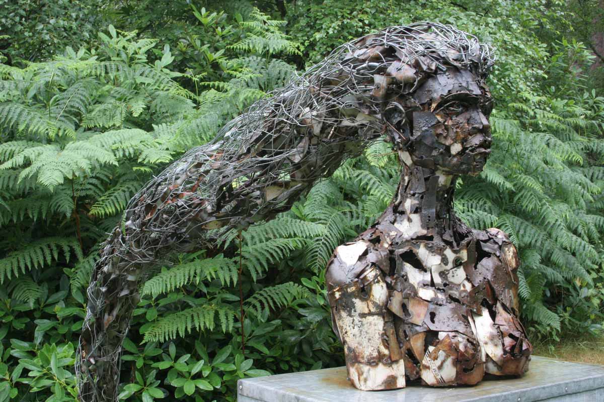 A figurative welded steel sculpture of a bust of a woman with long wiry hair.