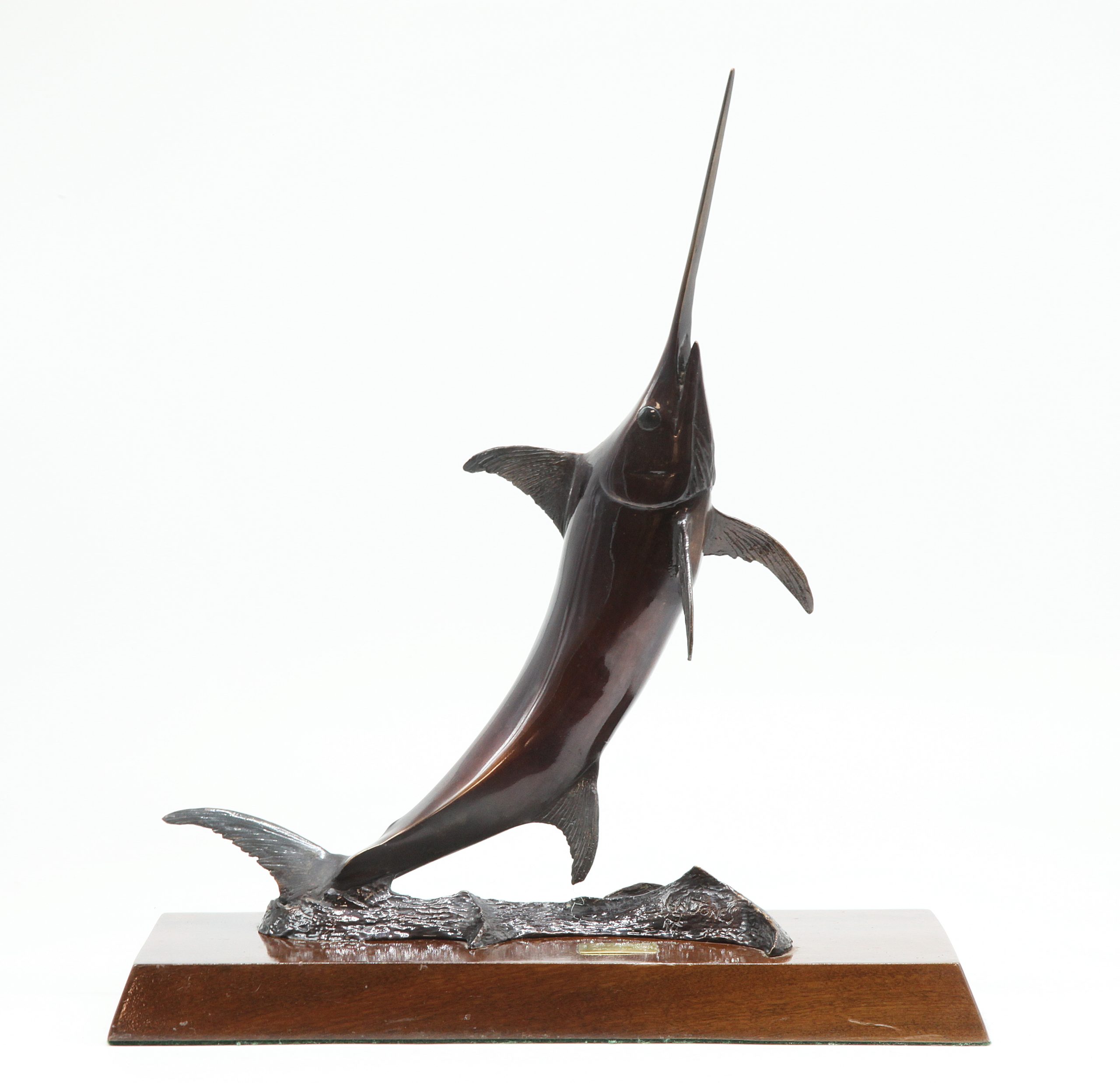 A bronze sculpture of a broadbill swordfish, mounted onto a slab of wood.