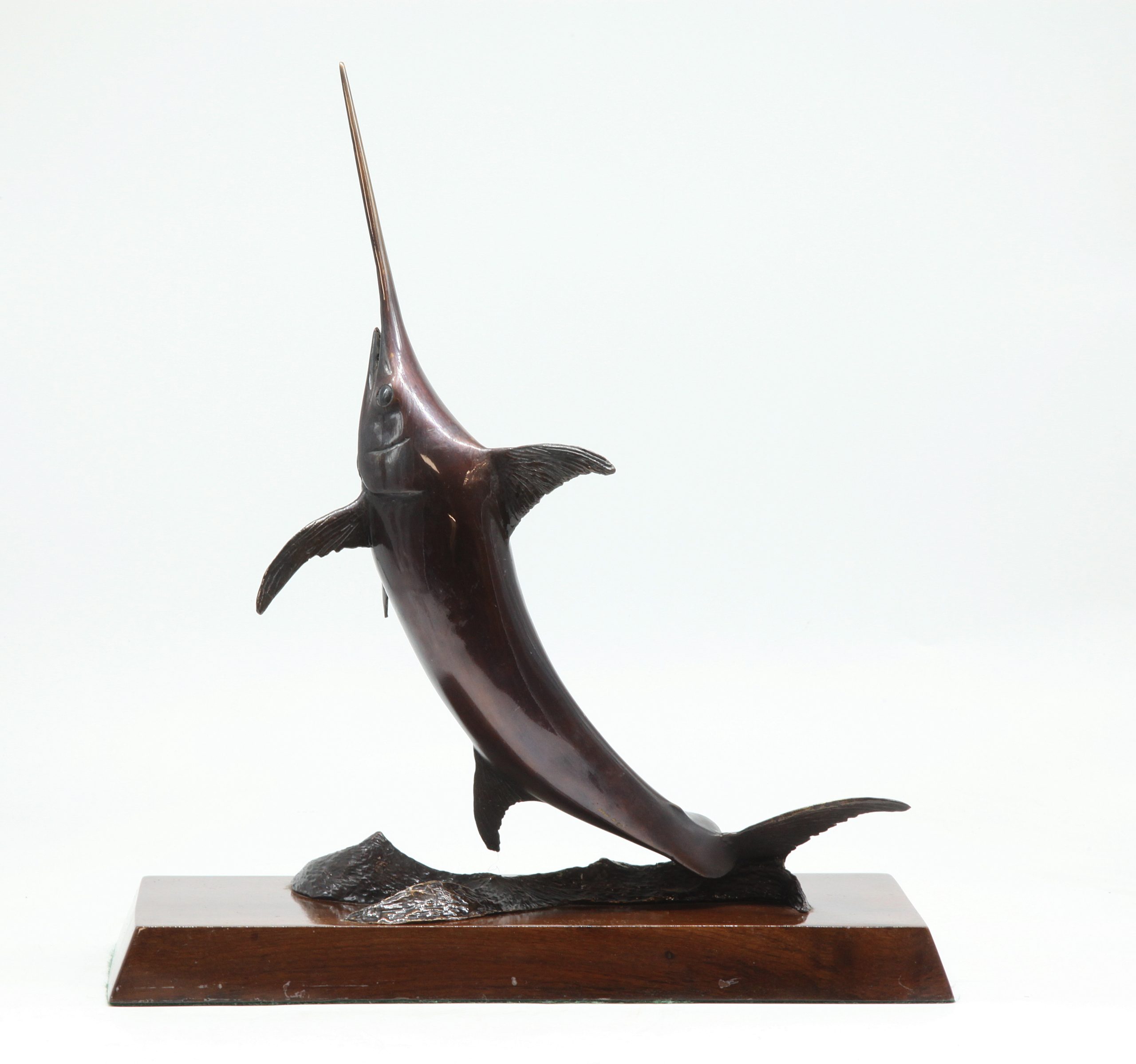 A bronze sculpture of a broadbill swordfish, mounted onto a slab of wood.