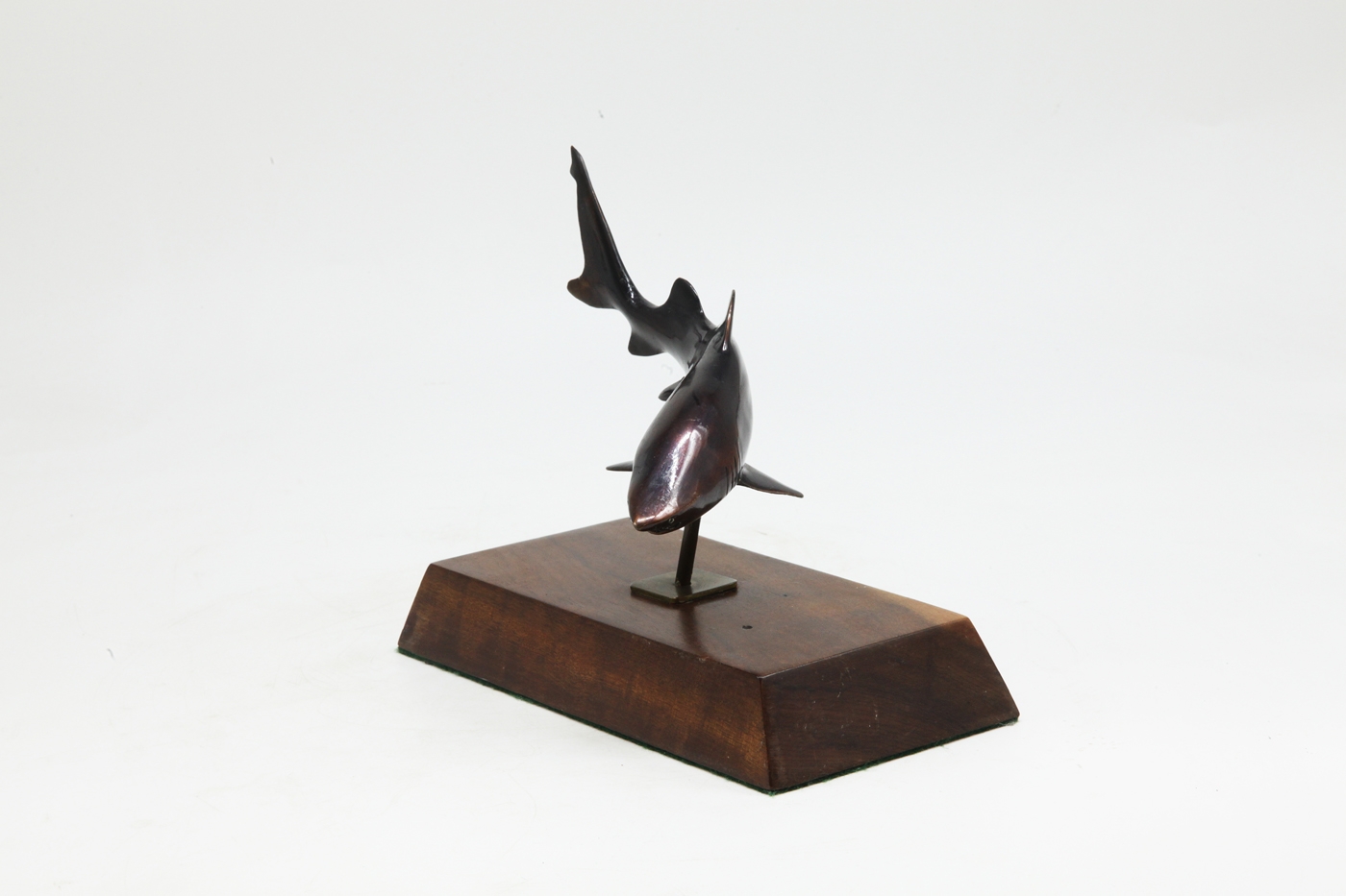 A bronze sculpture of a shark mounted onto a block of wood.