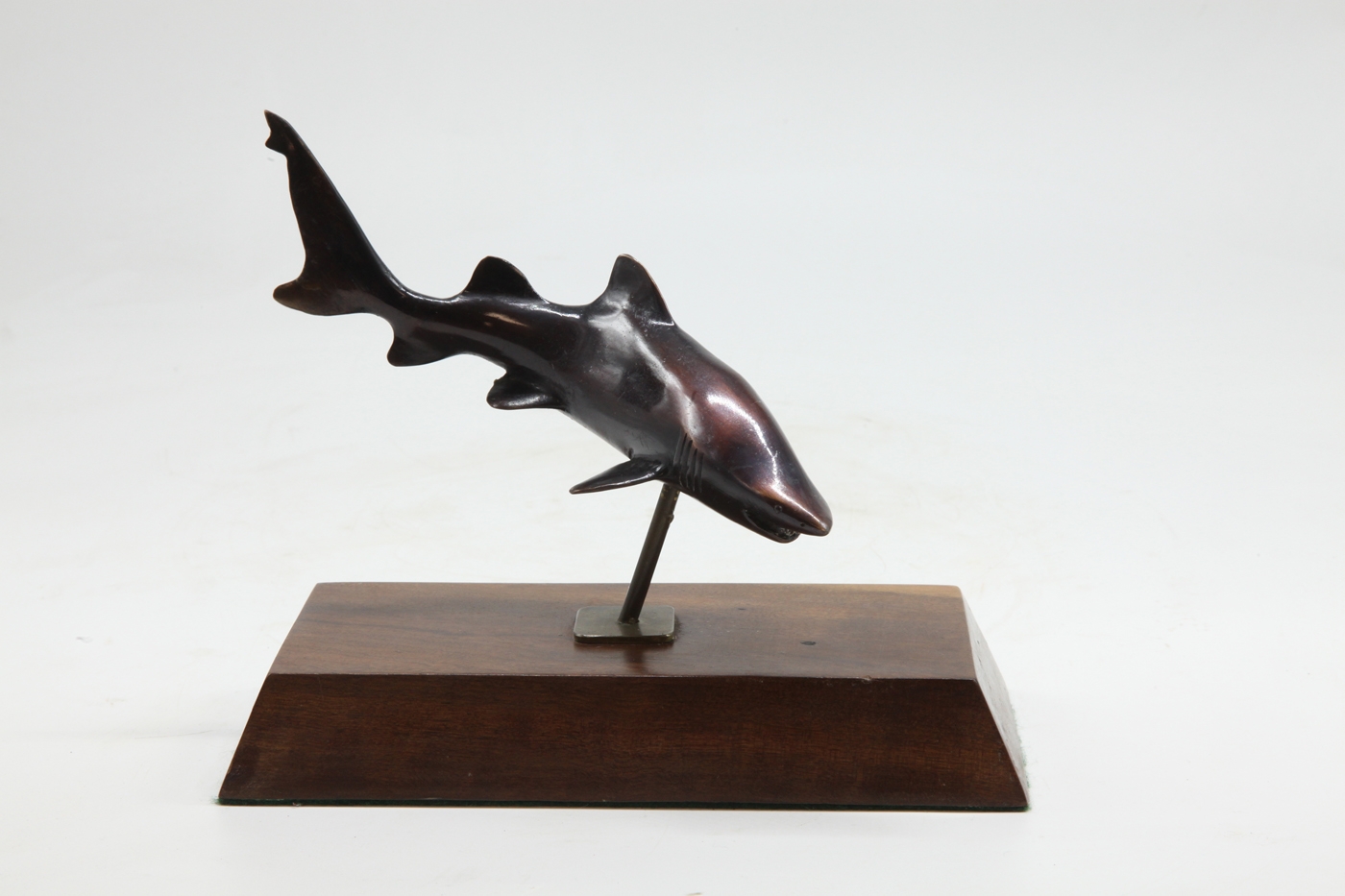 A bronze sculpture of a shark mounted onto a block of wood.
