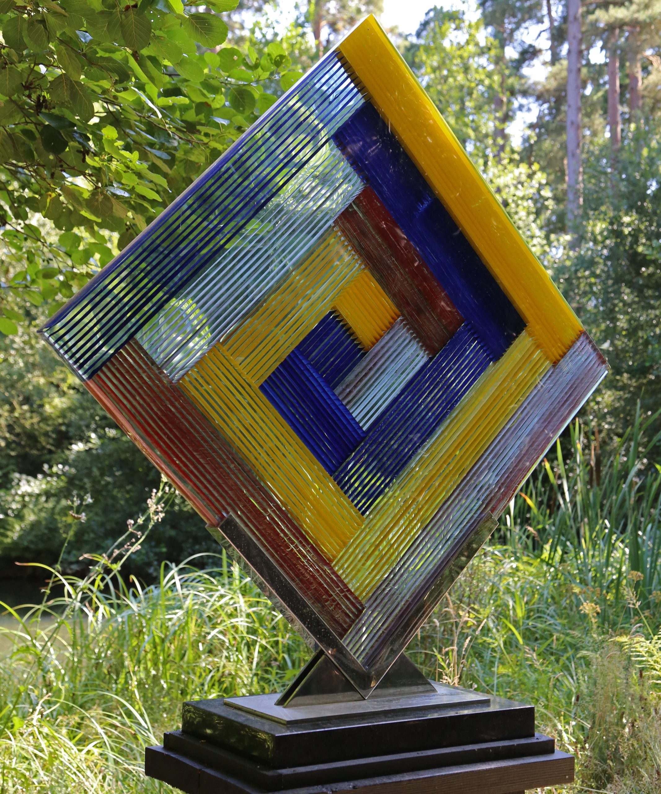 A abstract kiln formed glass sculpture of a square formed of strips of coloured glass.
