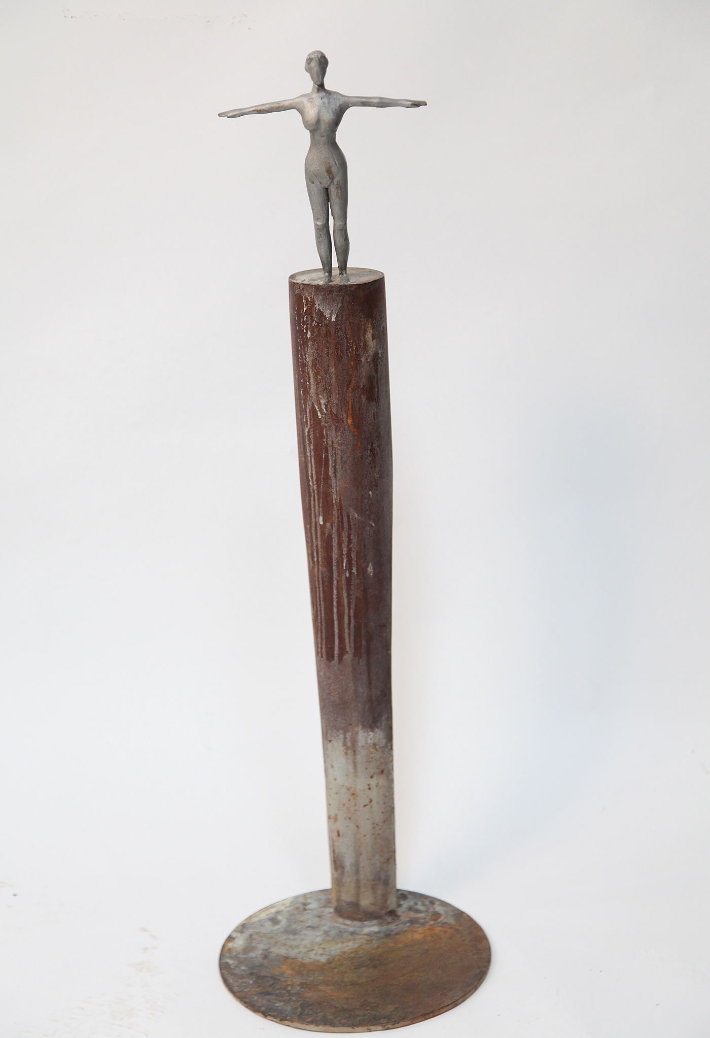 A figurative steel and wooden sculpture of a figure on top of a tall pillar.
