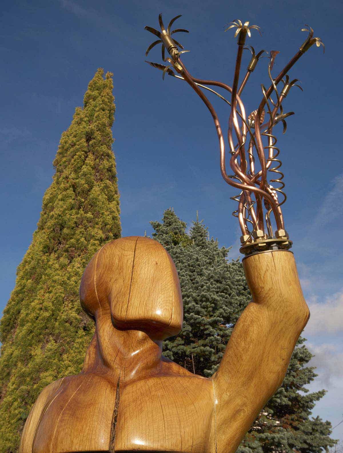 A abstract wood and copper sculpture of a figure with metal wires coming from their arm.