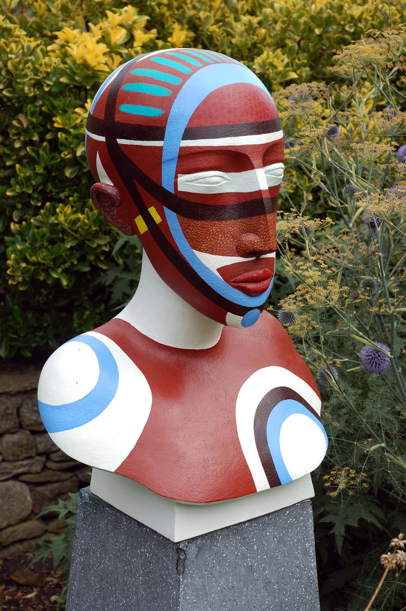 A figurative stoneware sculpture of a portrait bust of a person painted with various colours.