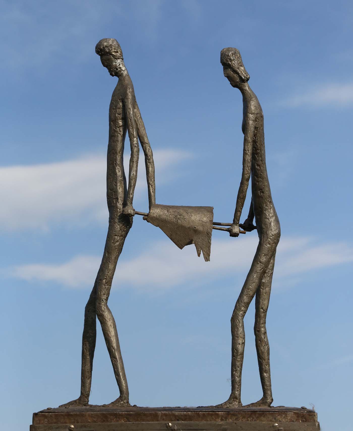 A figurative bronze sculpture of a man and a woman carrying something between them.
