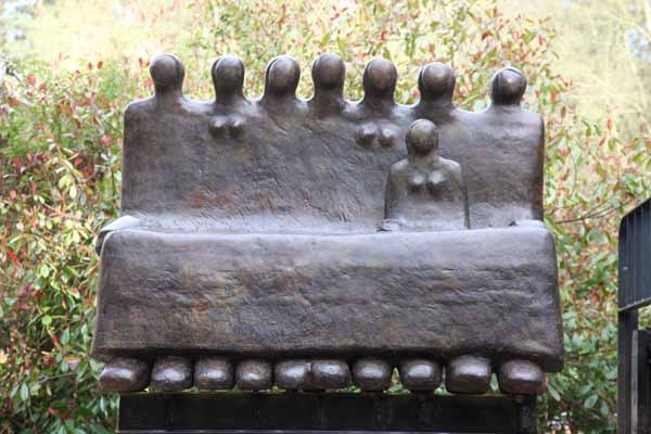 A figurative bronze sculpture of a group of people sitting together on a bench.