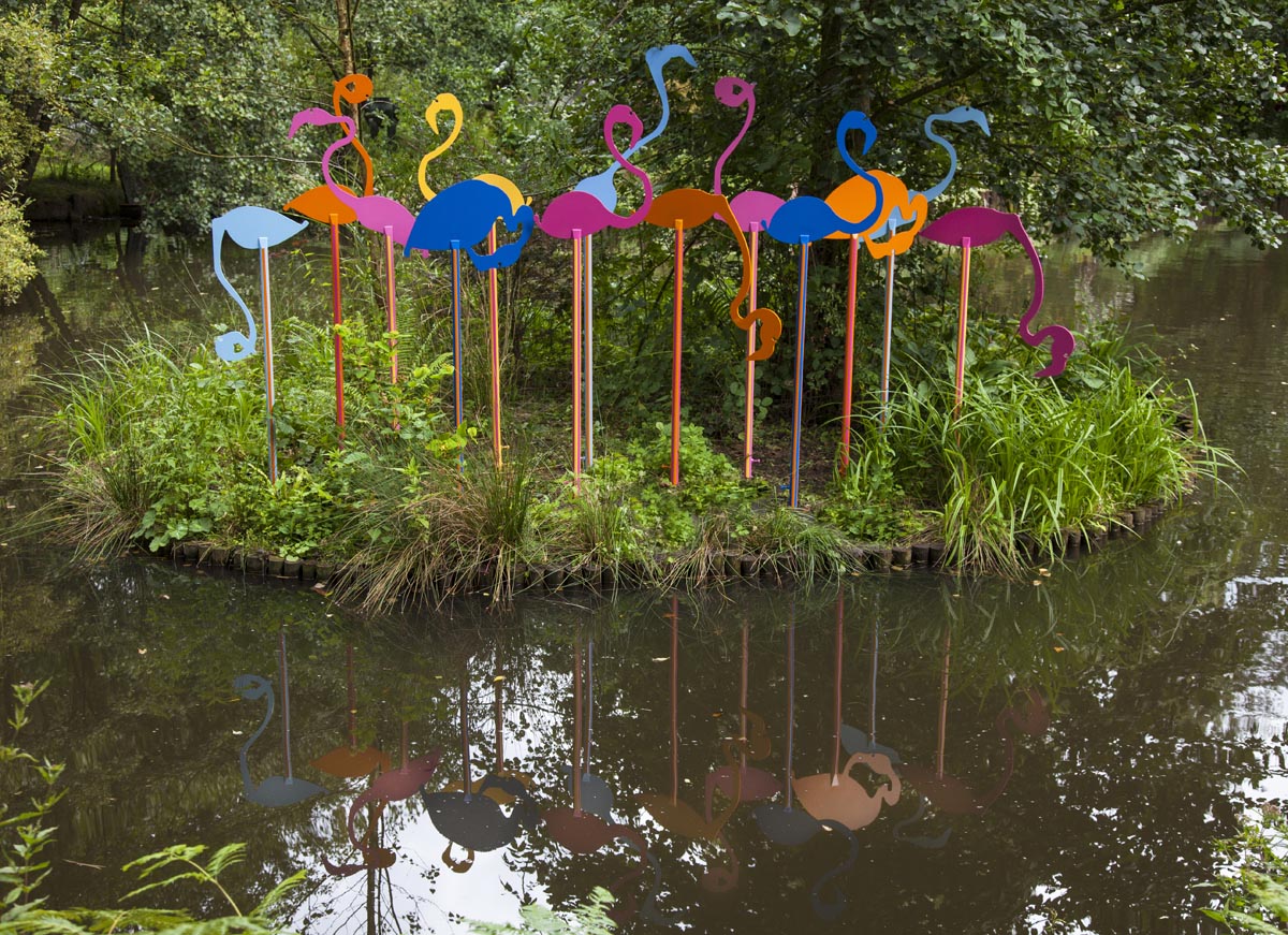A contemporary steel sheet sculpture of a flock of flamingos painted various colours.