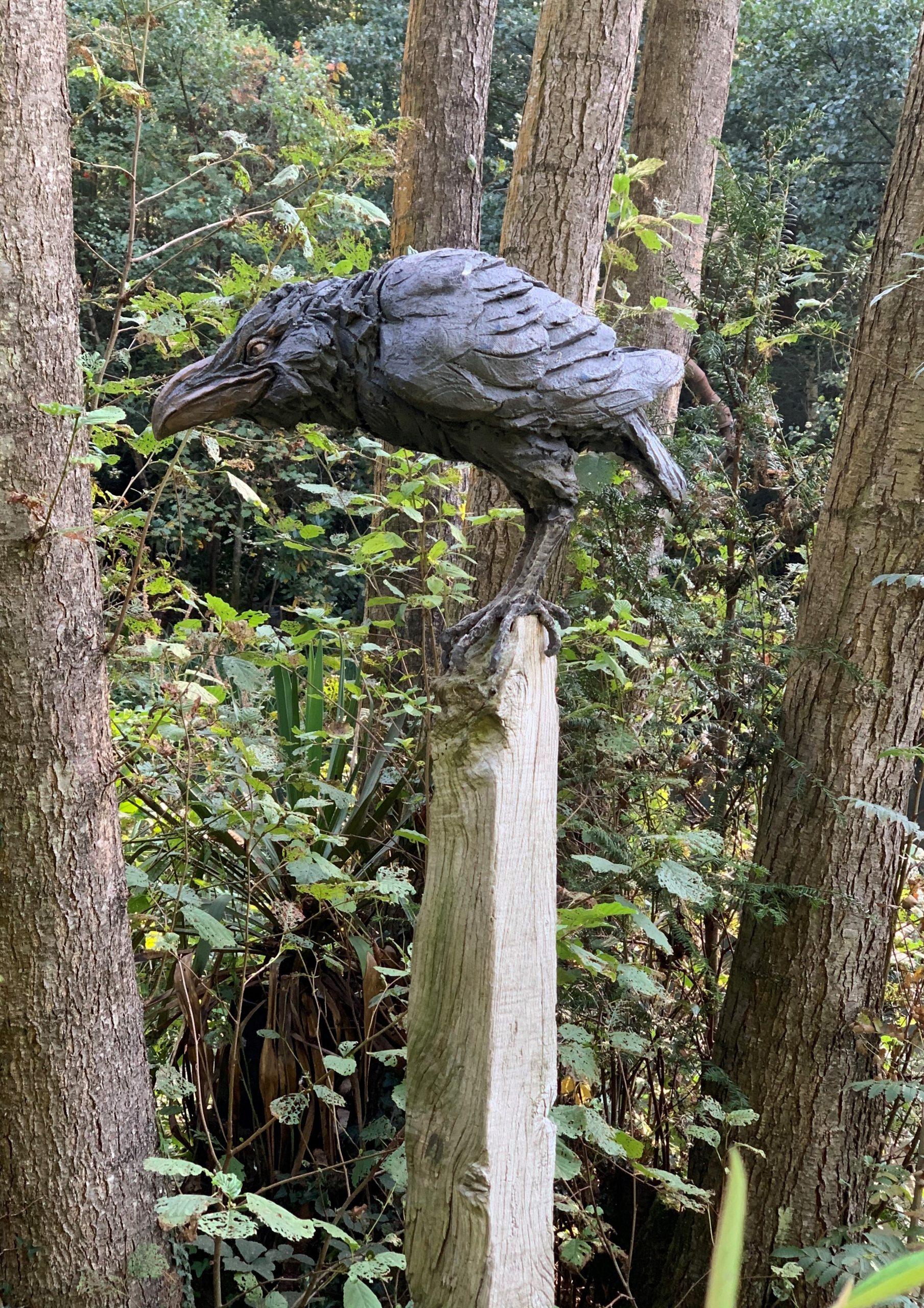 A figurative stoneware sculpture of a crow perched on top a stick.