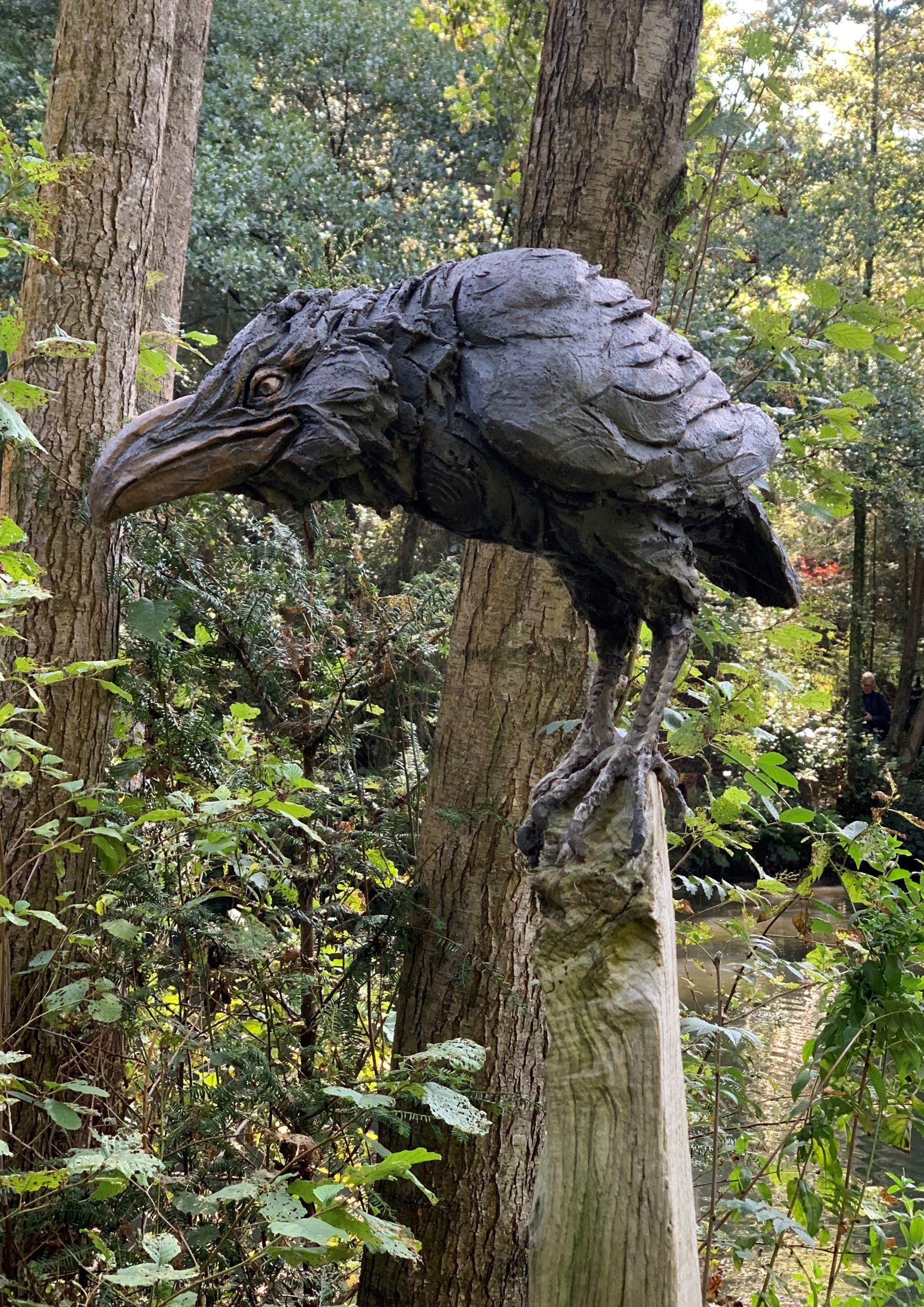 A figurative stoneware sculpture of a crow perched on top a stick.