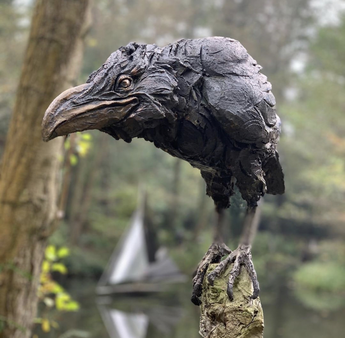 A figurative stoneware sculpture of a crow perched on top a stick.