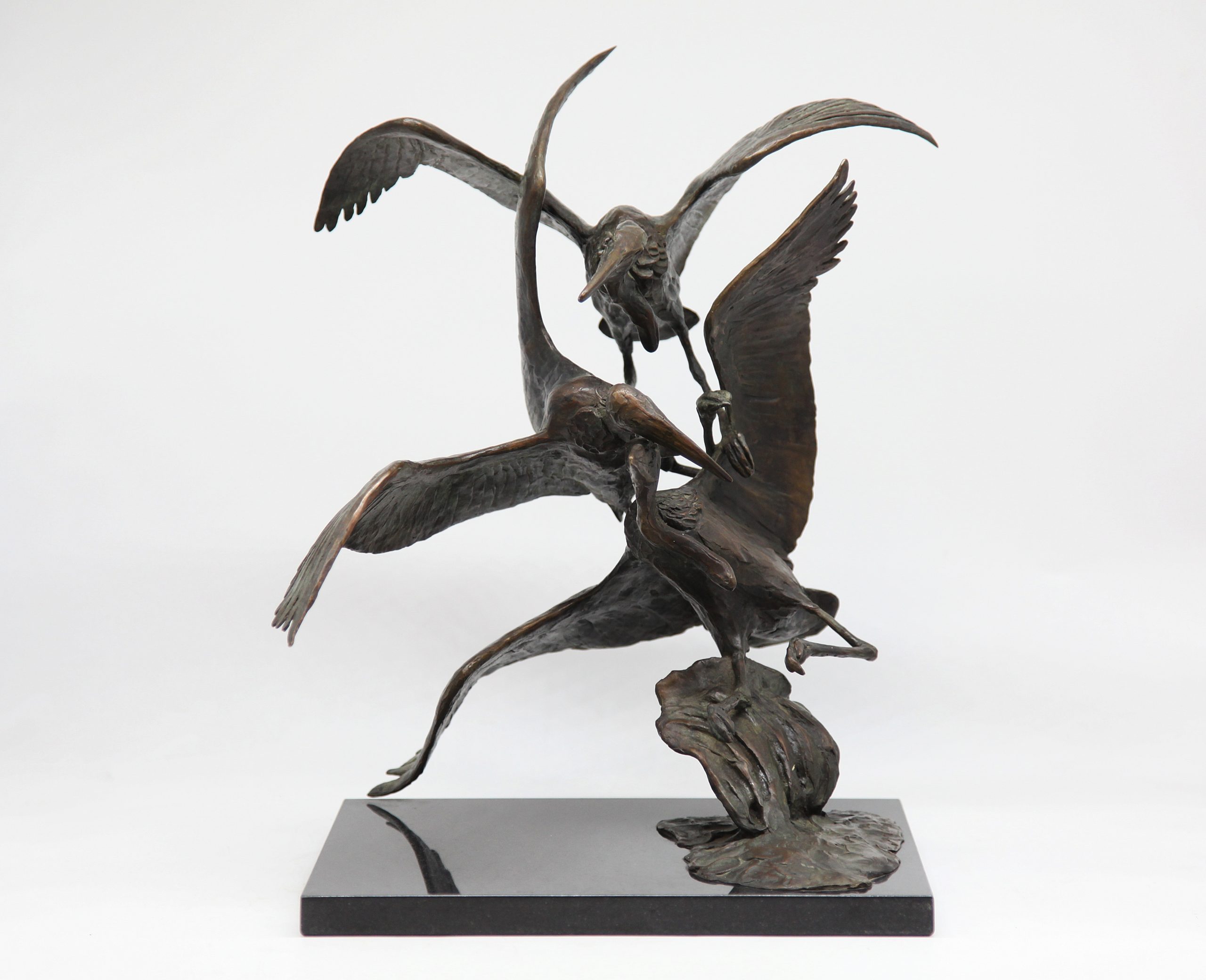 A bronze sculpture of three pelicans in flight, mounted onto a slab of black marble.