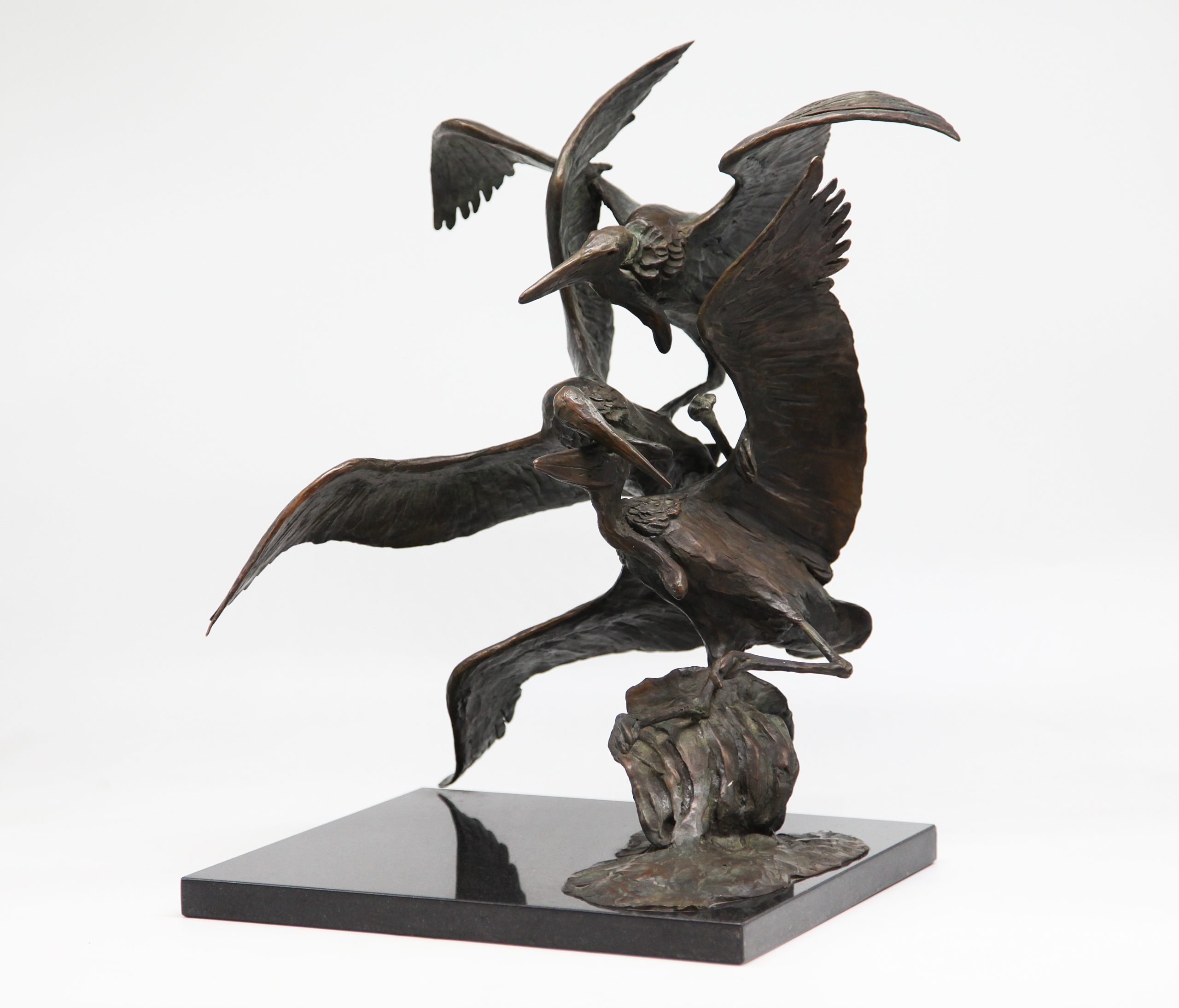 A bronze sculpture of three pelicans in flight, mounted onto a slab of black marble.