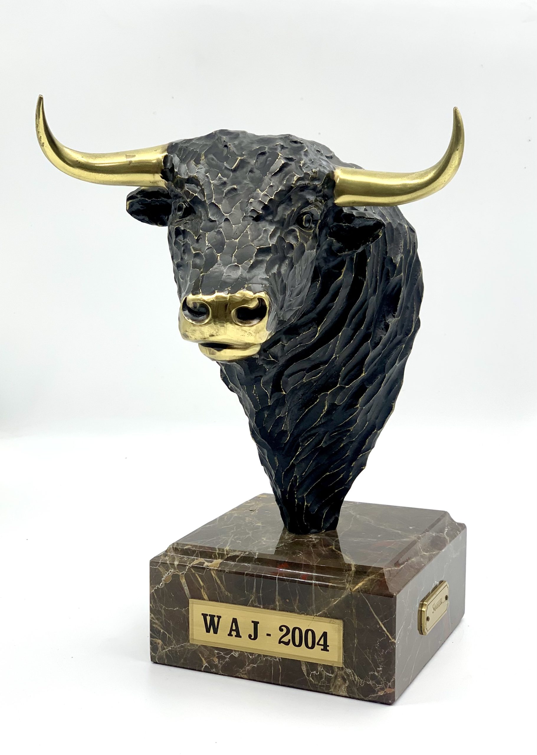 A figurative bronze sculpture of a bulls head with golden horns and nose, mounted onto a block of marble.