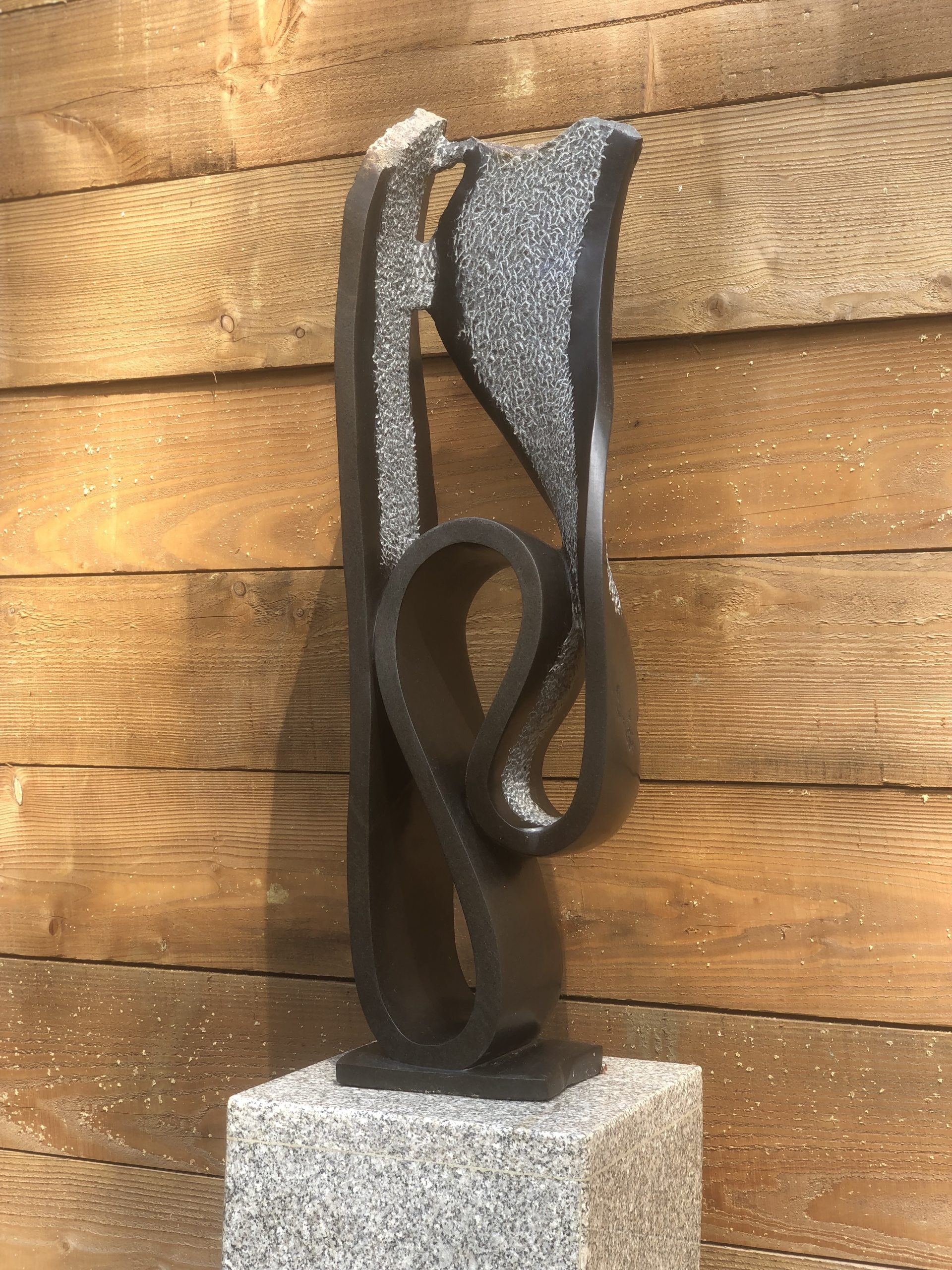 An abstract Shona springstone sculpture depicting a curving and swirling shape, some areas are polished and some are left natural