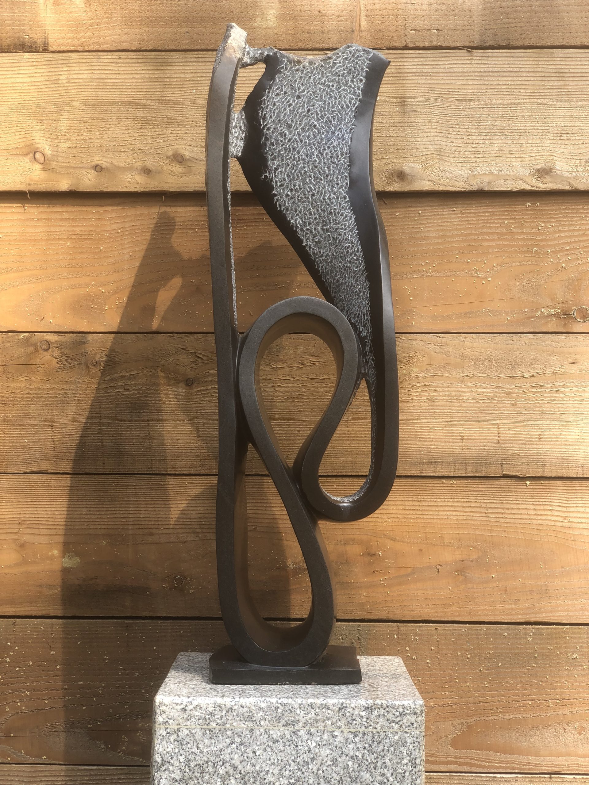 An abstract Shona springstone sculpture depicting a curving and swirling shape, some areas are polished and some are left natural