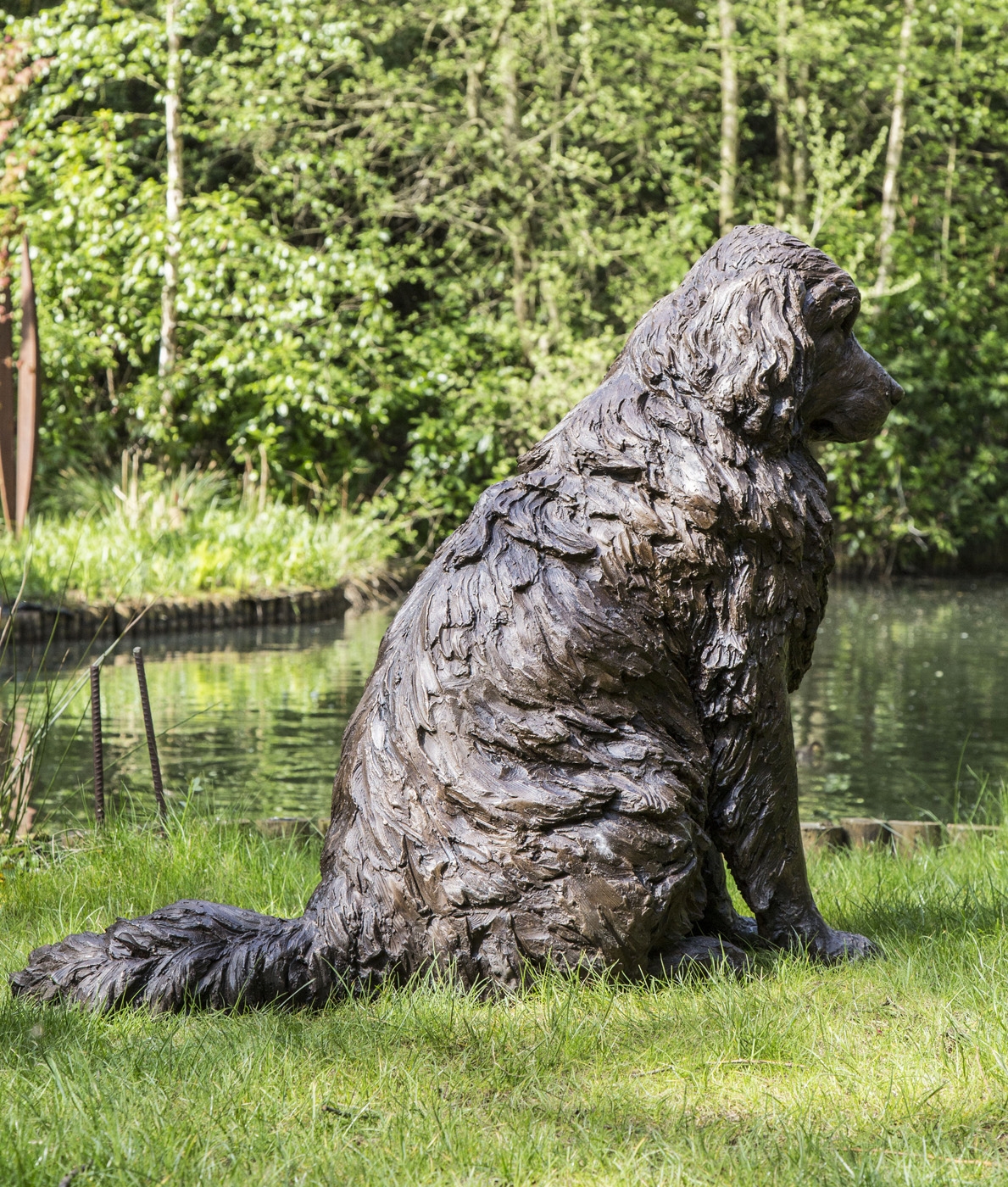 A realism bronze resin sculpture of a newfoundland dog sitting.