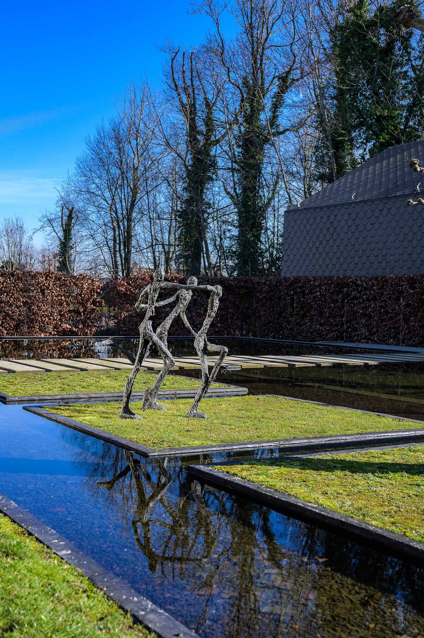 A figurative bronze sculpture of a group of three figures running and holding hands.