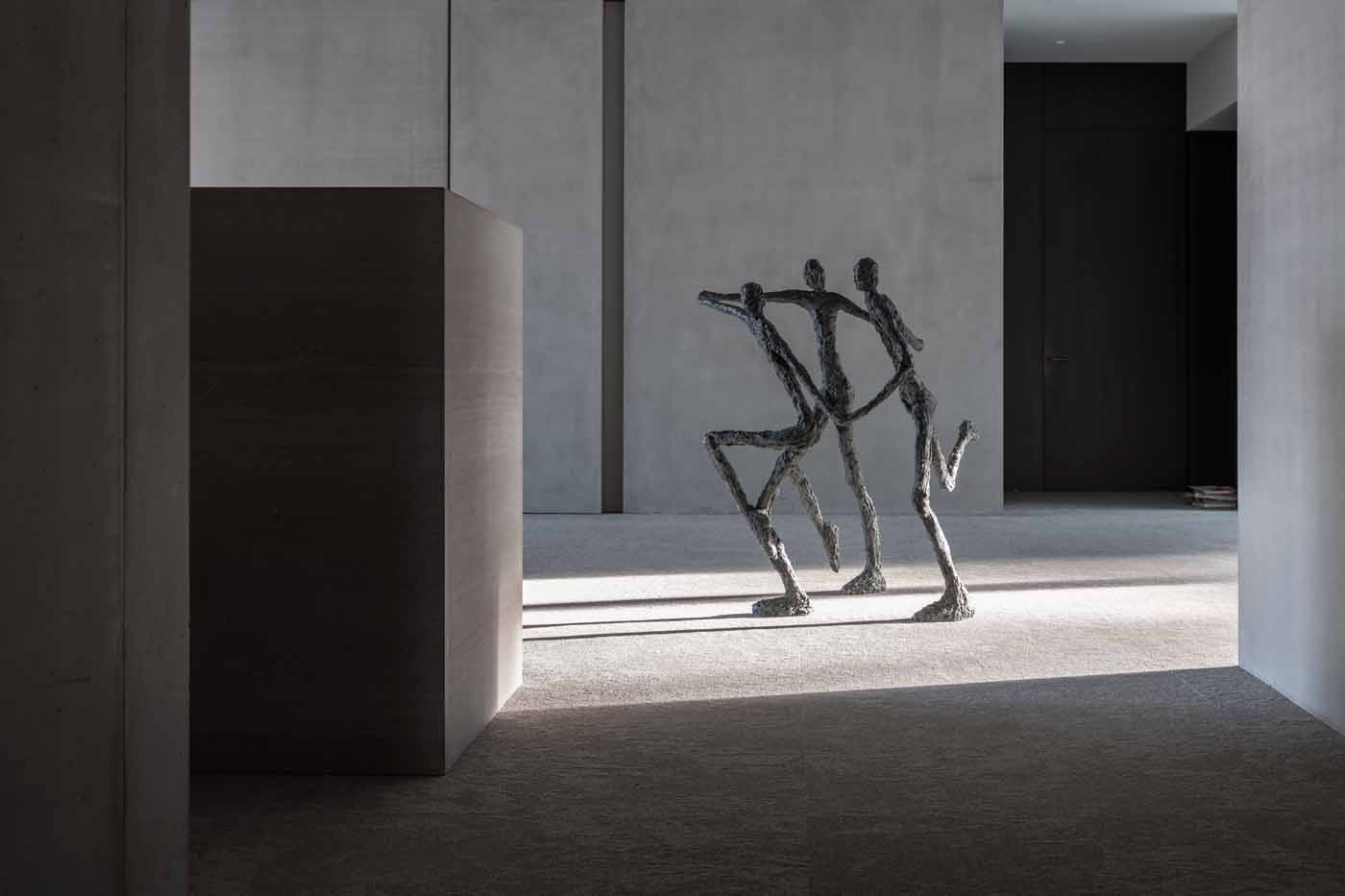 A figurative bronze sculpture of a group of three figures running and holding hands.