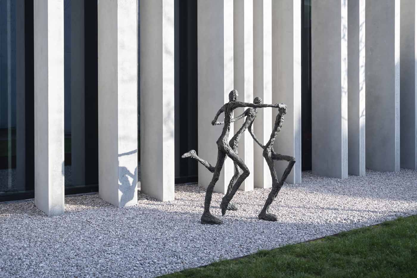 A figurative bronze sculpture of a group of three figures running and holding hands.