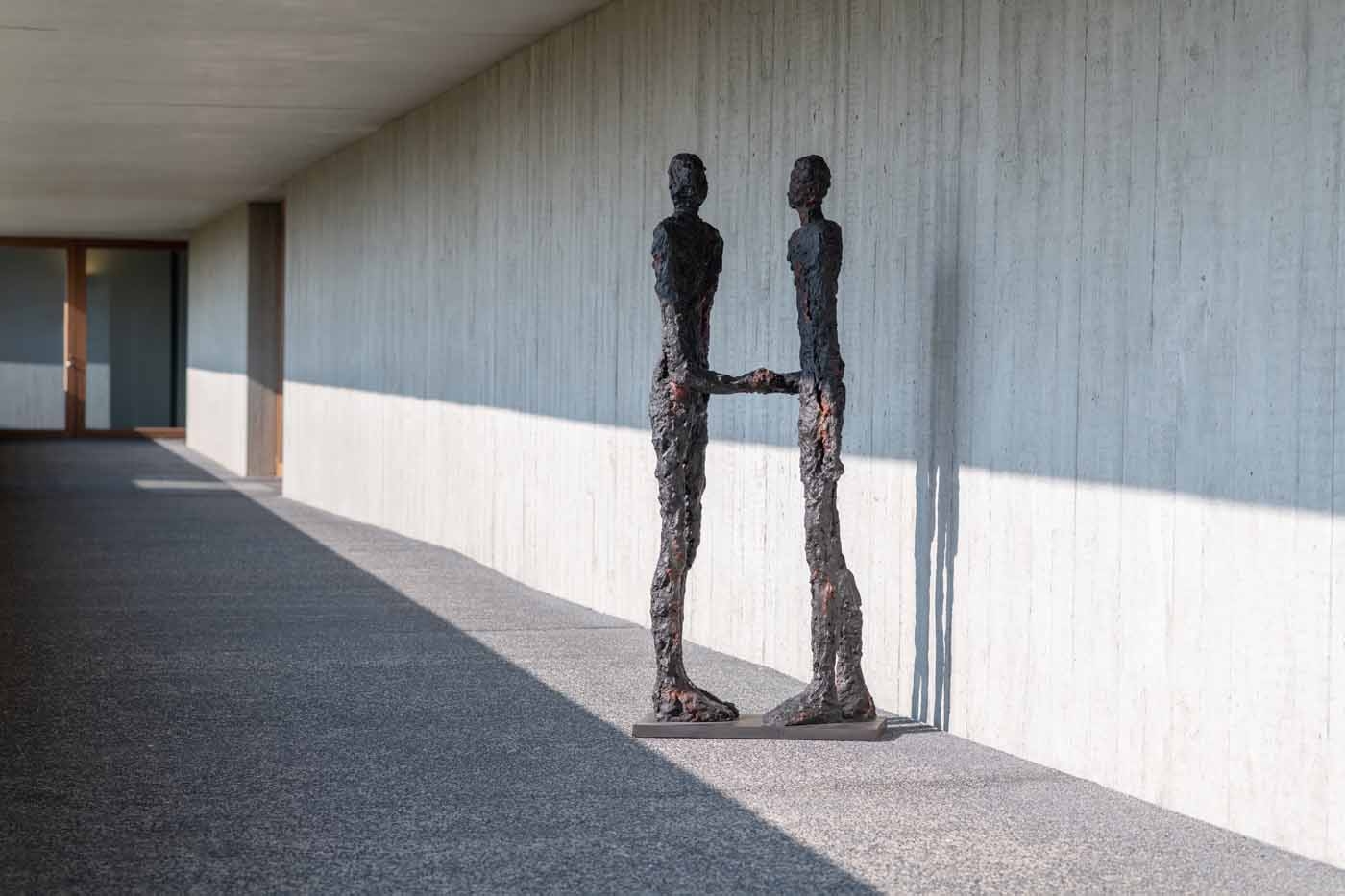 A figurative bronze sculpture of two figures facing each other and shaking hands.