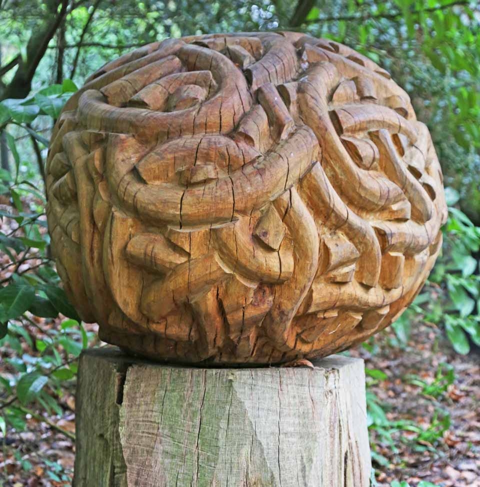 A abstract wooden sculpture of a ball with various twists and turns all over it.