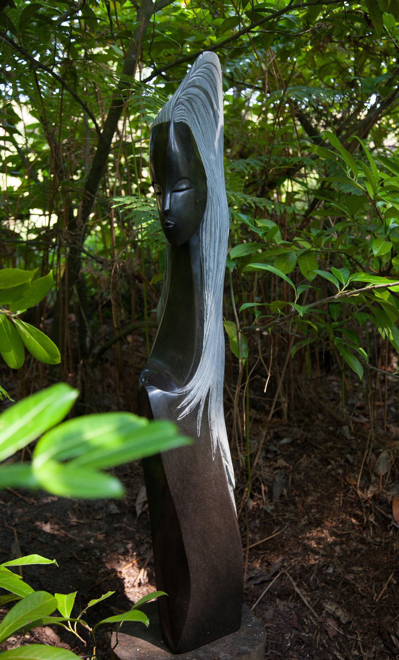 A Shona sculpture of a woman's bust with her head facing sideways and her long hair going down her back. Made of Springstone.