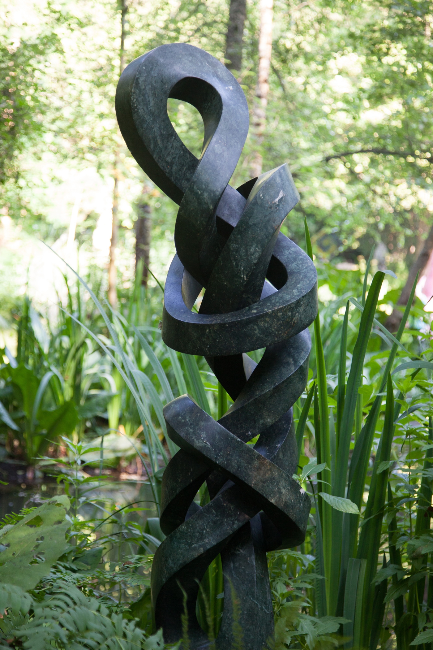 An abstract Shona sculpture of tall twirling shapes, intertwined within themselves. Made of Opal stone.