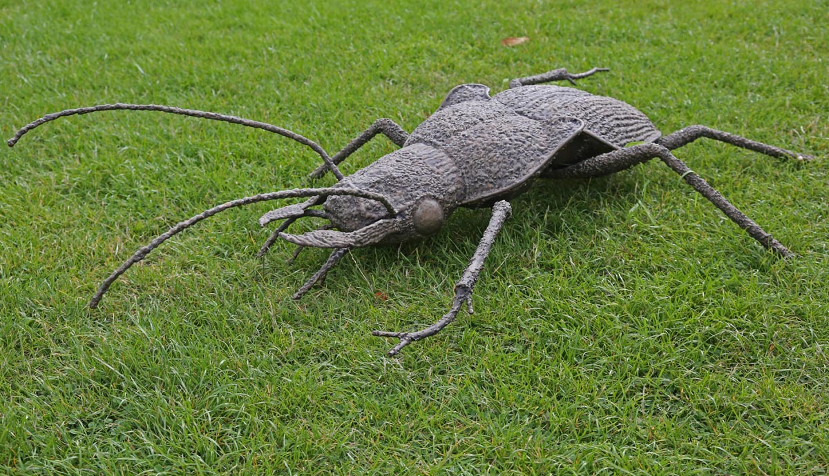 A figurative metal sculpture of a violet ground beetle crawling on the ground.