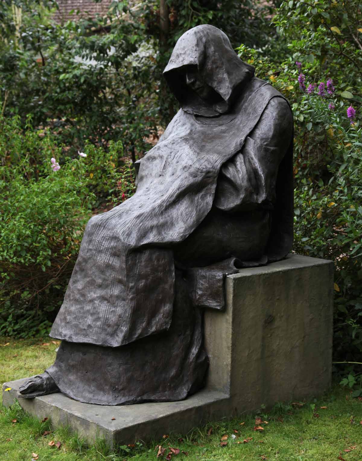 Larger-than-life bronze sculpture of a sitting monk, wearing a cloak with hood up