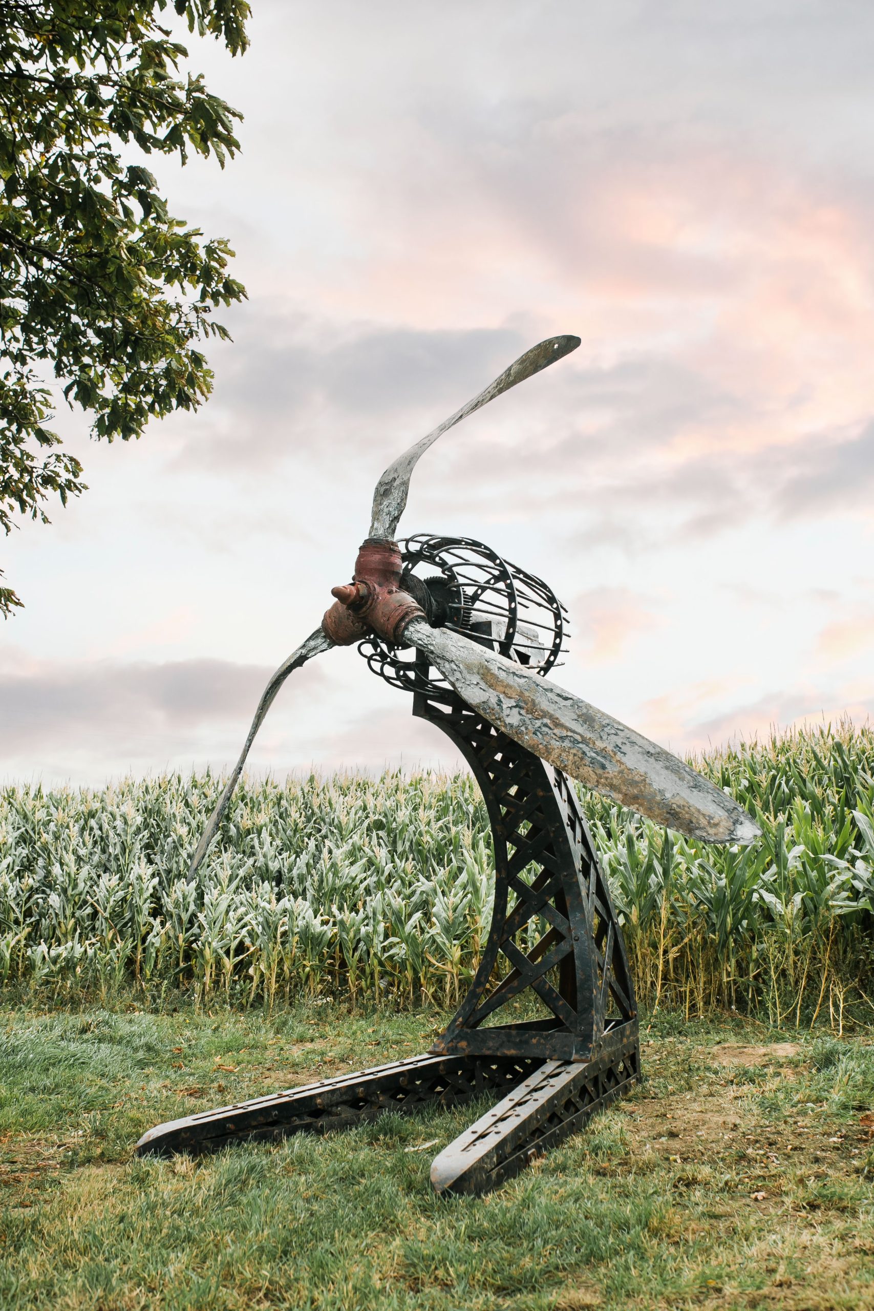 A architectural found object sculpture of a plane propeller mounted onto a metal frame.