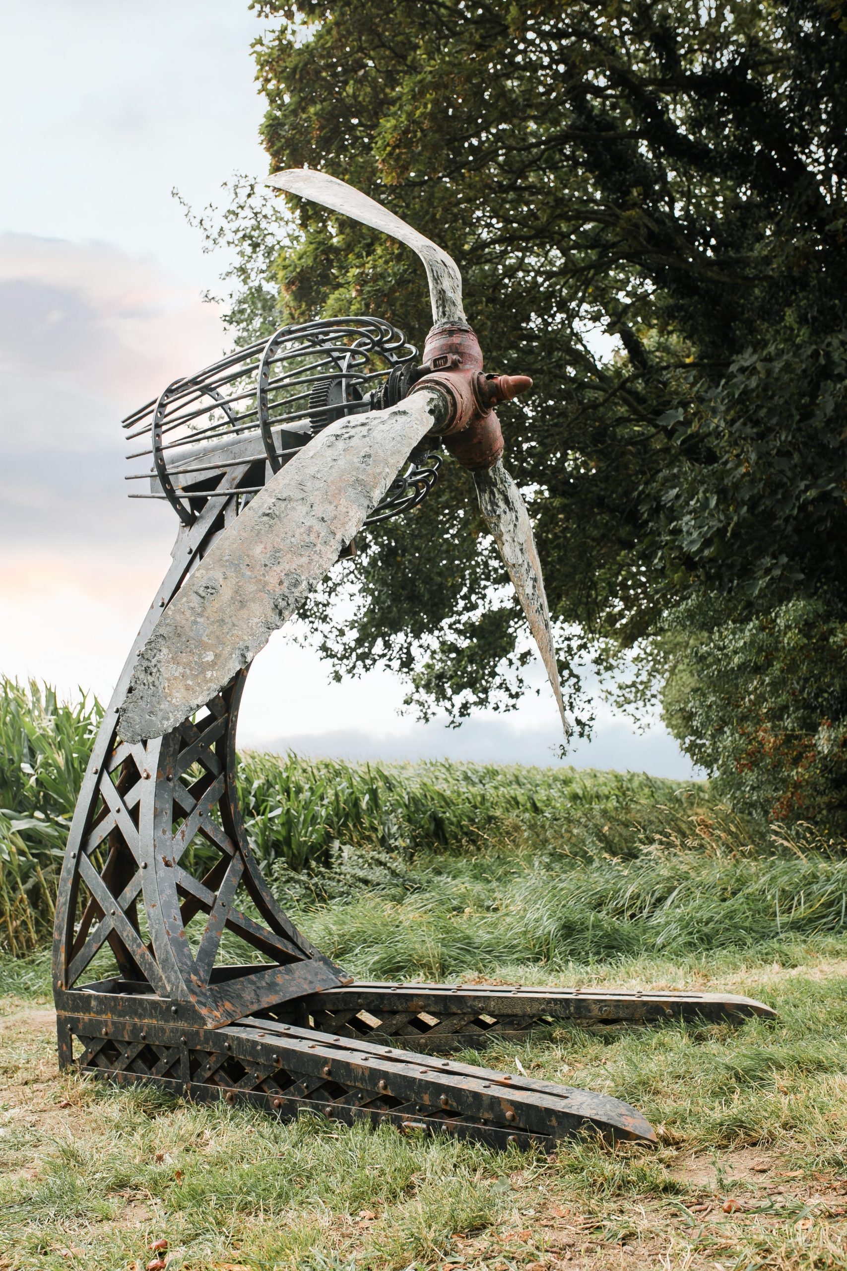 A architectural found object sculpture of a plane propeller mounted onto a metal frame.