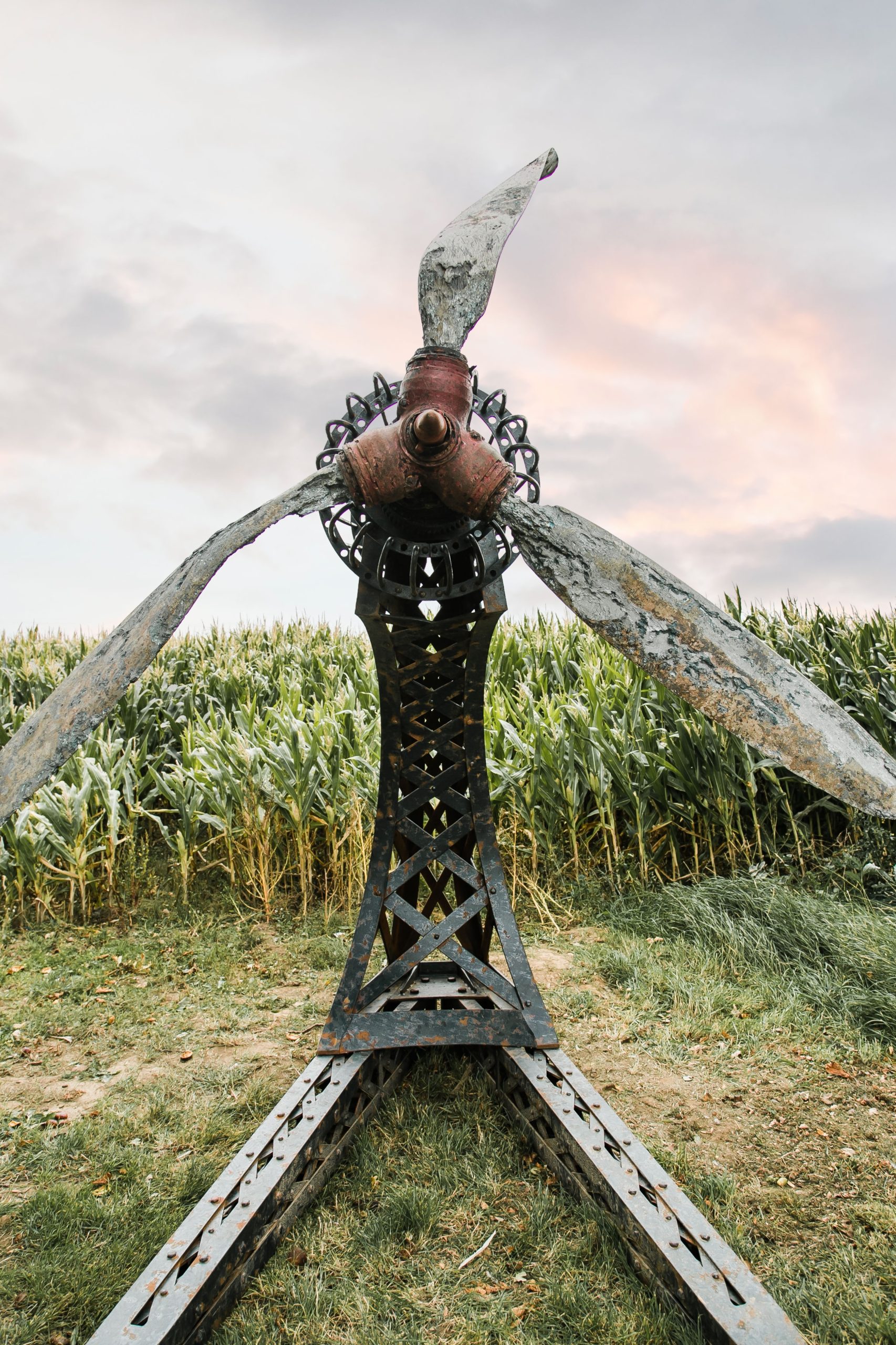 A architectural found object sculpture of a plane propeller mounted onto a metal frame.